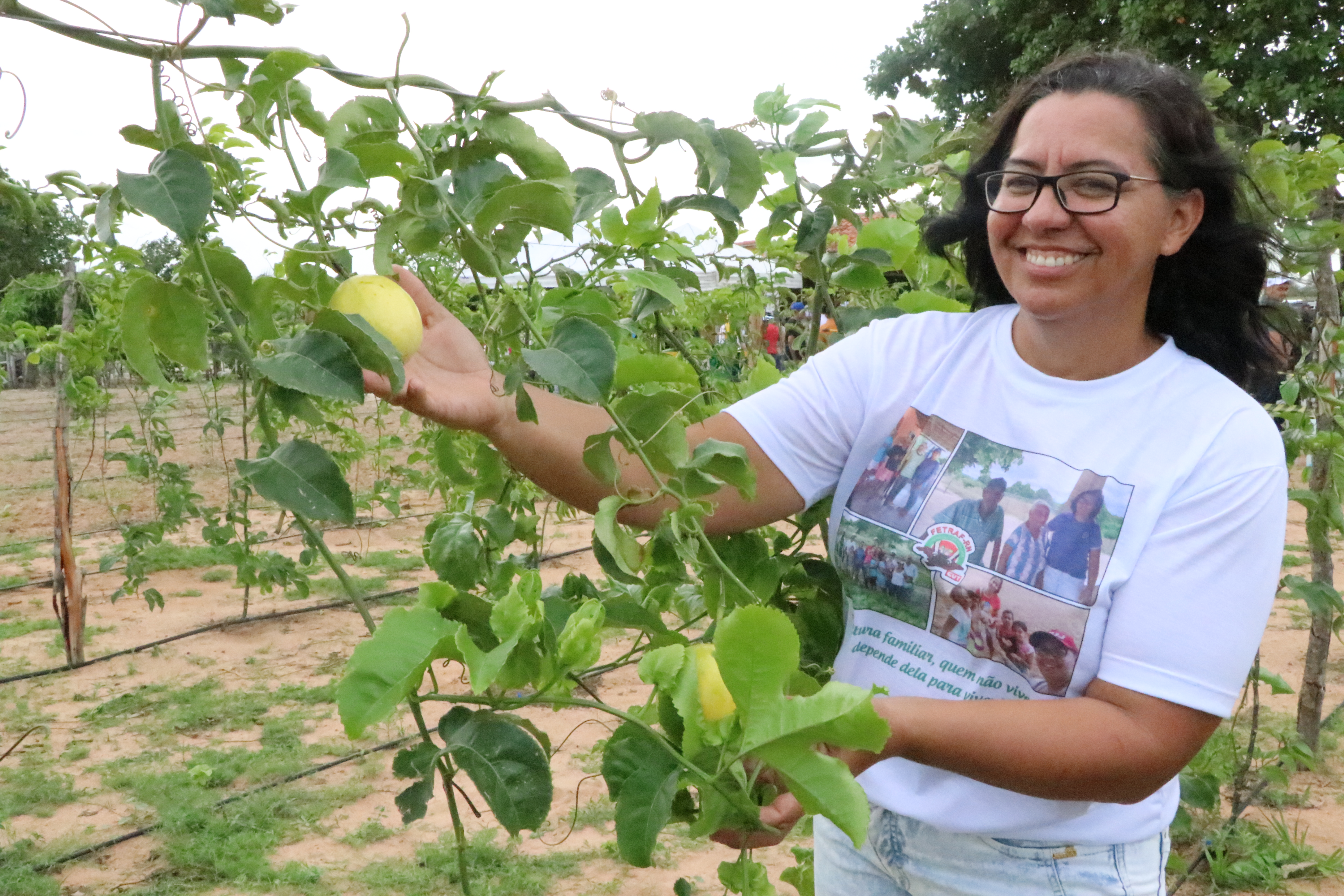 Mulher negra sorrindo posa ao lado de pé de maracujá