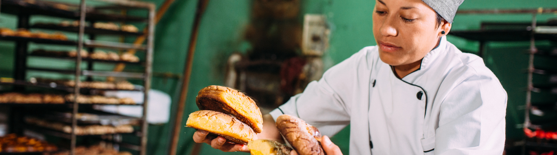 A imagem contém uma mulher segurando pães recém-saídos do forno na cozinha de uma padaria